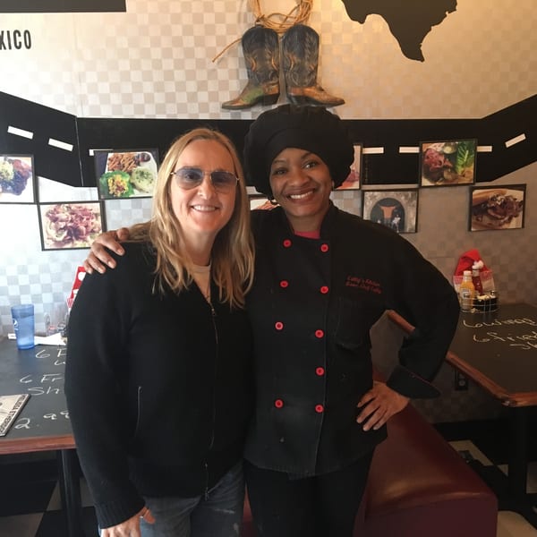 Cathy's Kitchen Executive Chef Cathy, in uniform, smiling with a customer in the dining area.