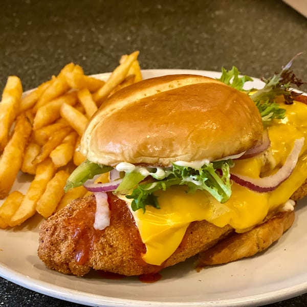 A crispy chicken sandwich with melted cheese, lettuce, red onion, and fries on a white plate.