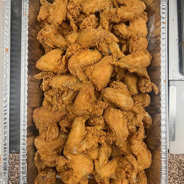 A large aluminum tray filled with crispy, golden-brown fried chicken wings from Cathy's Kitchen.