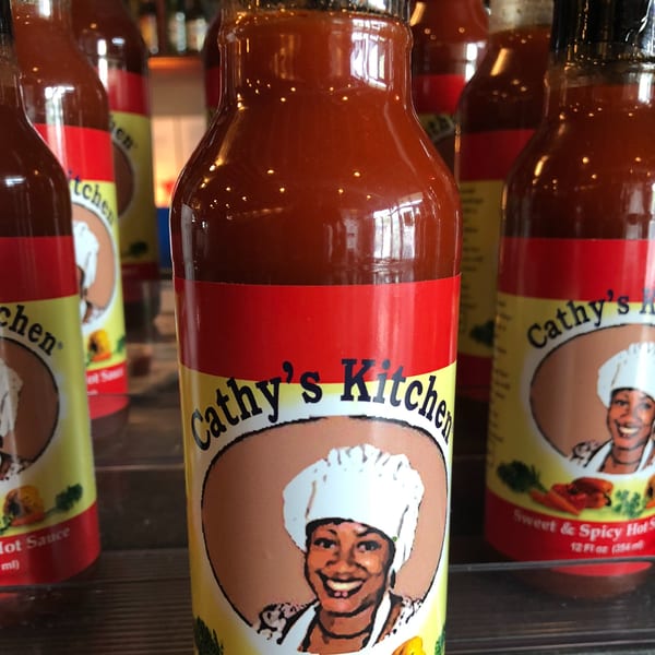 Bottles of Cathy's Kitchen Sweet & Spicy Hot Sauce with a smiling chef on the label.